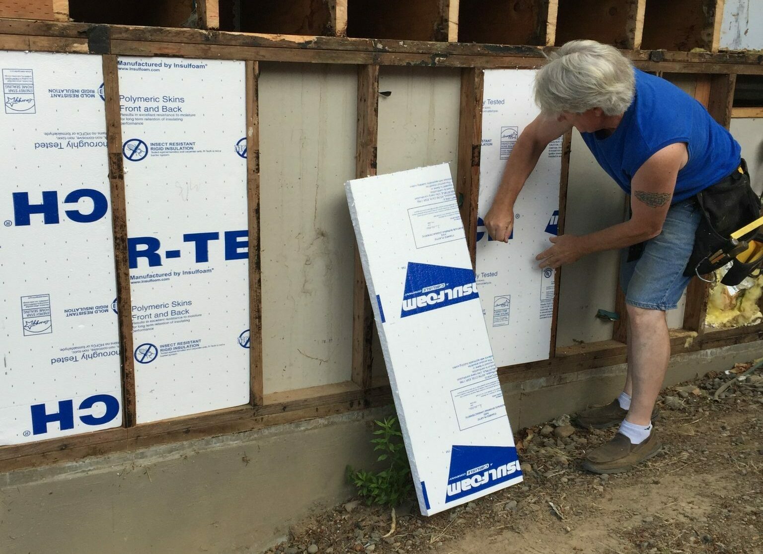Image of a man installing foam board insulation on the side of a home.